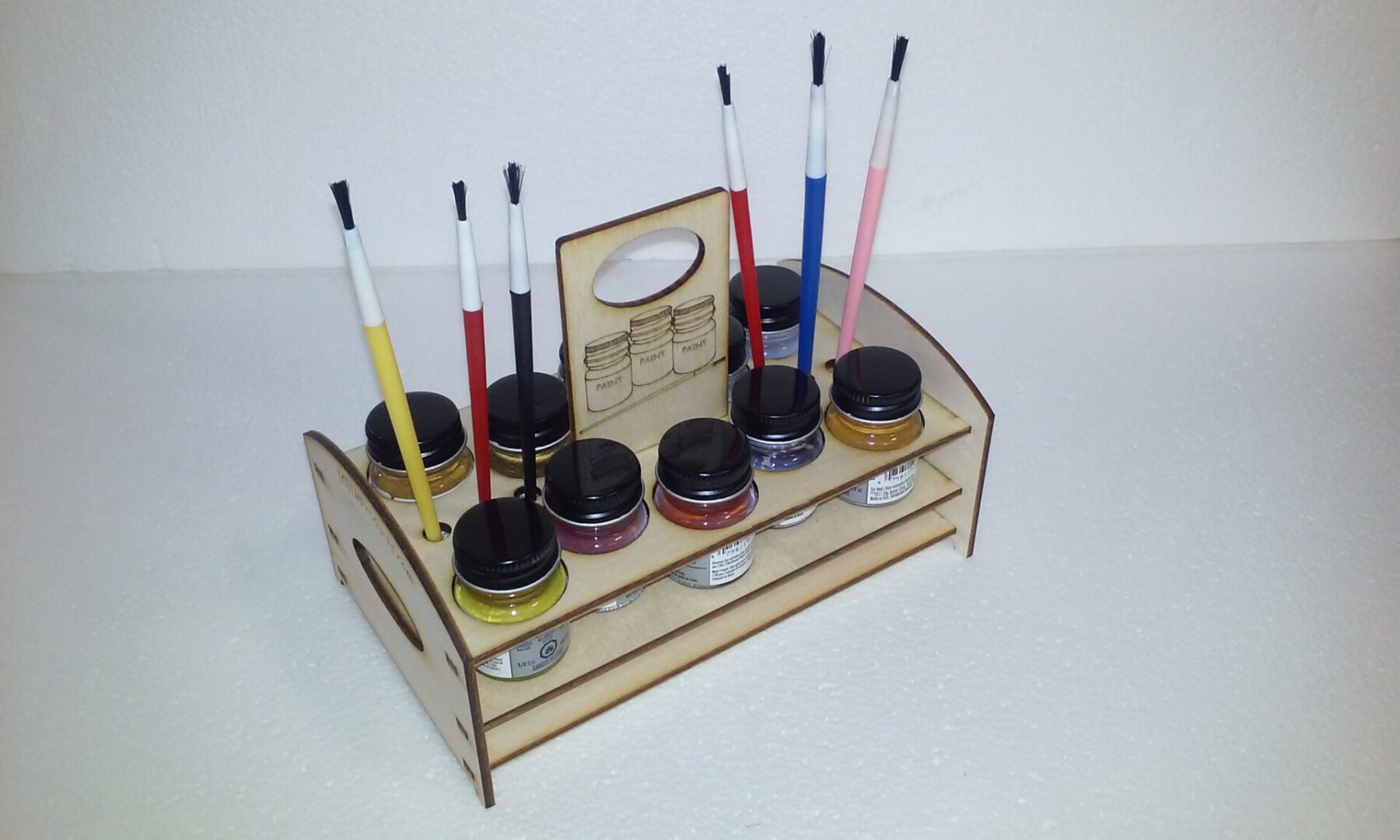 A wooden holder with paint brushes and paints on it.